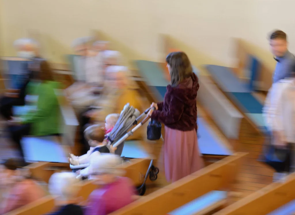 Mutter läuft in die Kirche mit dem Kinderwagen. Ein Junge hält sich am Kinderwagen, während seine kleine Schwester im Kinderwagen sitzt