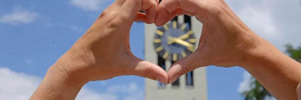 Hände formen ein Herz, durch welches man die Uhr der Comanderkirche sieht